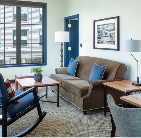 Modern living room with a brown sofa, blue door, wooden furniture, and a framed picture above the couch in a Newport RI hotel.