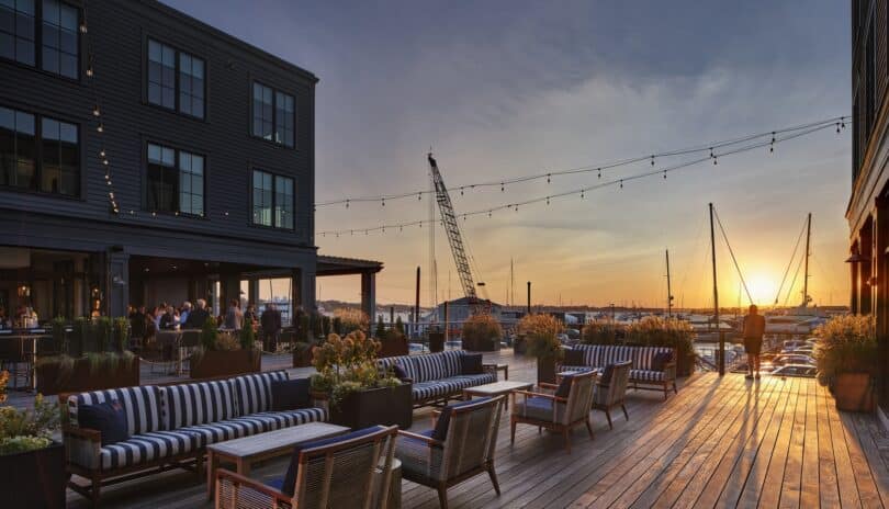 Sunset view at a waterfront hotel in Newport with outdoor seating, string lights, and yachts in the distance.
