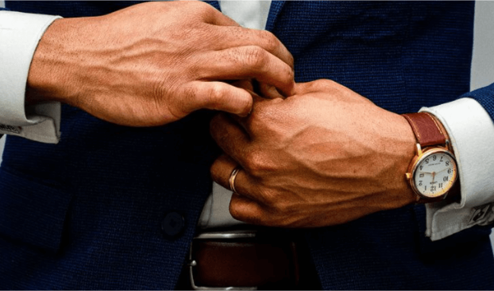 Close-up of a man in a blue suit adjusting his cuff, with a wristwatch visible on one arm, ready for a stay at one of the hotels in Newport RI.