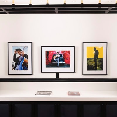 Four framed photographs displayed on a white wall in a Newport RI hotel, each capturing different couples in various poses, with a lighting track above and a shelf below holding a book.