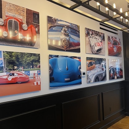 Wall decorated with framed photographs of vintage cars in various colors displayed in a Newport RI hotel interior setting with modern lighting.