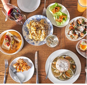 A variety of dishes on a wooden table at one of the hotels in Newport RI, including pasta, seafood, and salads, paired with glasses of wine and juice.