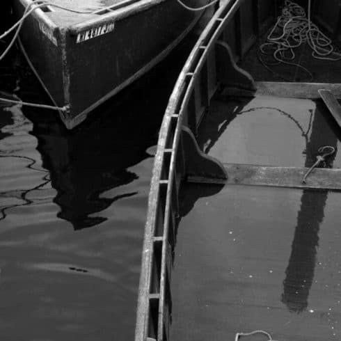 Black and white photo of a submerged boat with visible ladder alongside another boat near Newport RI hotel, reflecting in calm water.