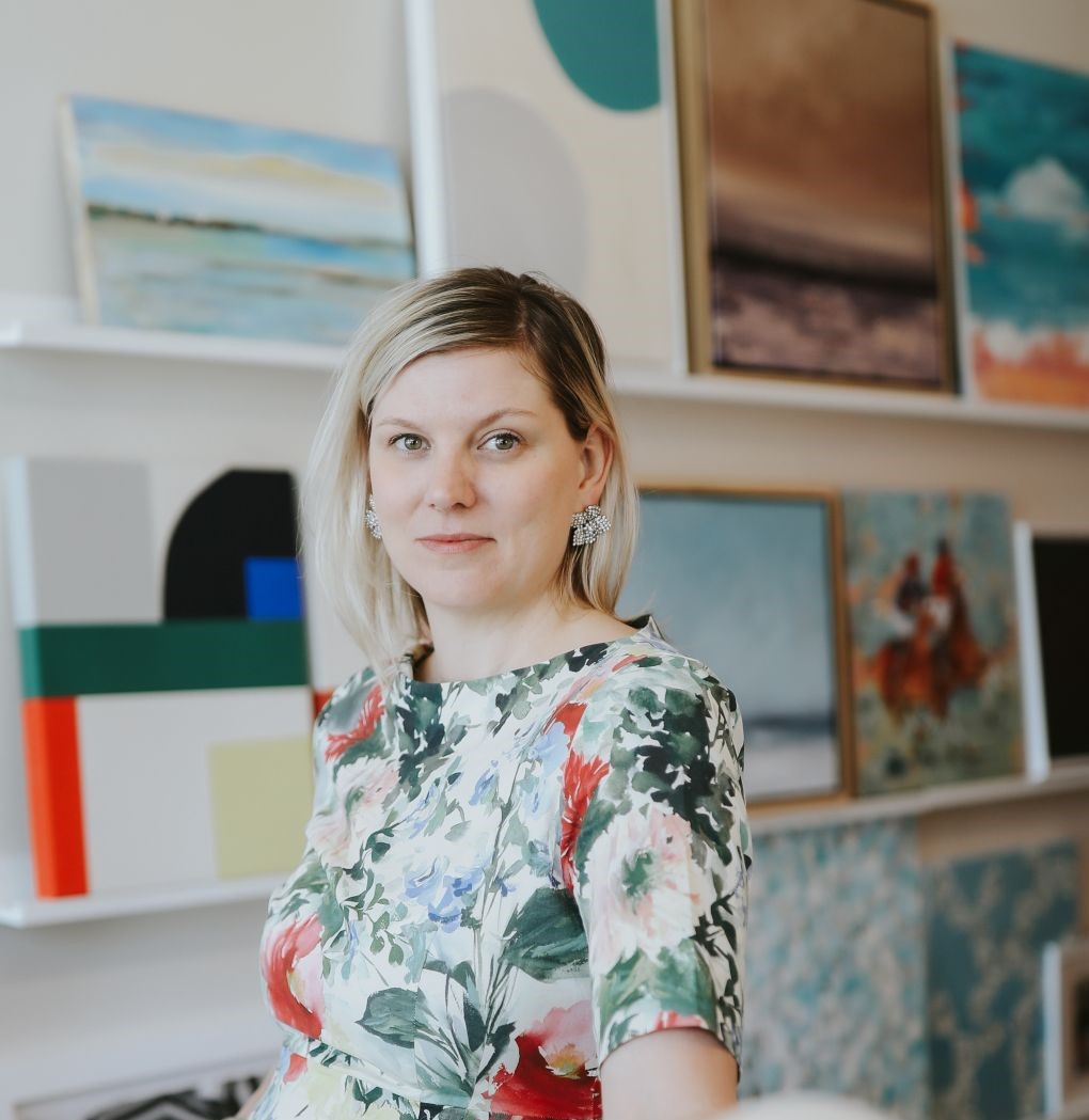 A woman in a floral dress standing in an art gallery surrounded by colorful paintings in a Newport RI hotel.