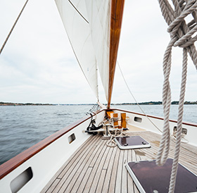 View from the deck of a sailboat with white sails, clear skies, and open water visible near Newport RI.