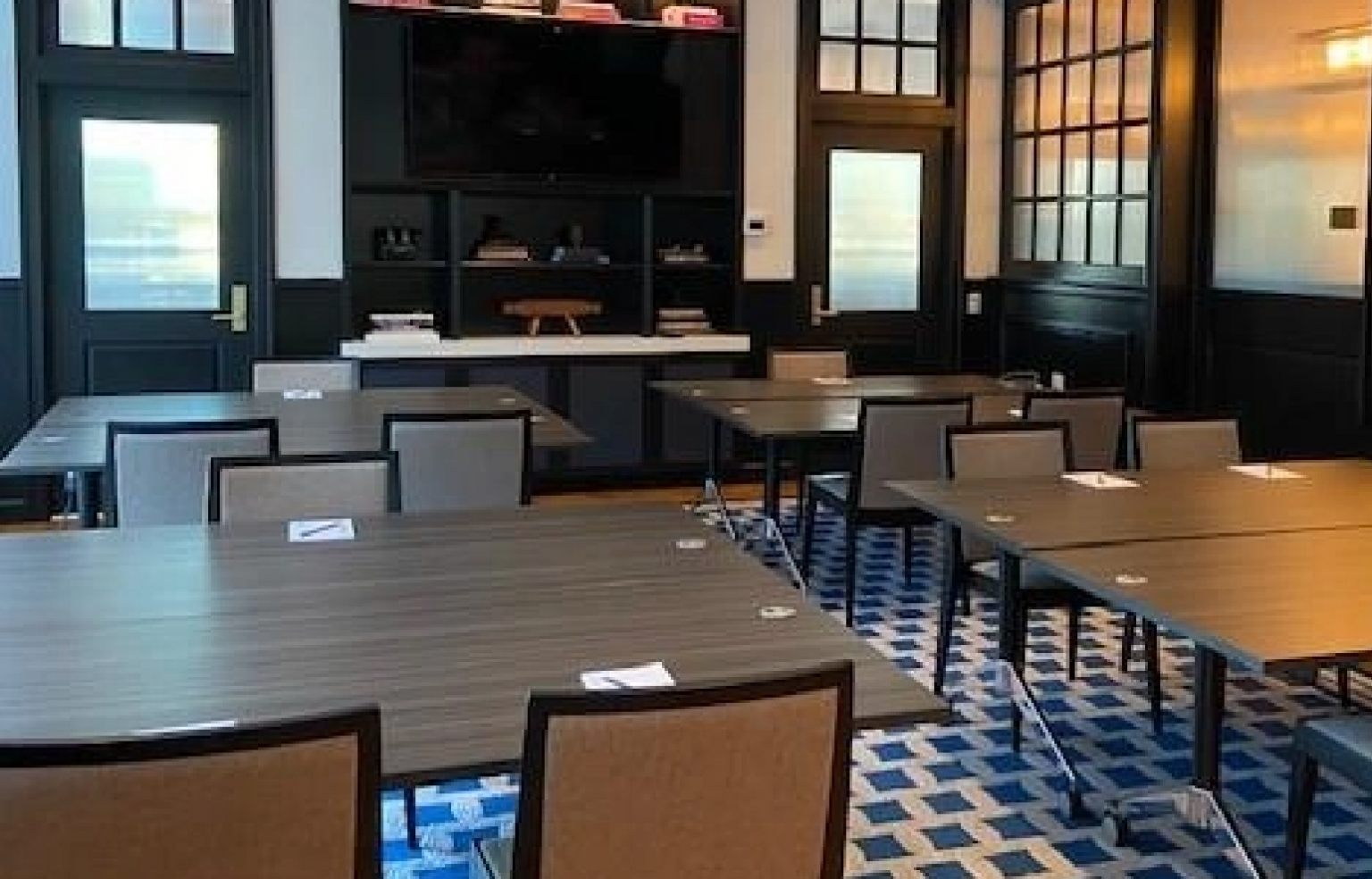 Modern conference room in a Newport, RI hotel with long tables, grey chairs, stylish blue carpet, and a bar area with shelves in the background.