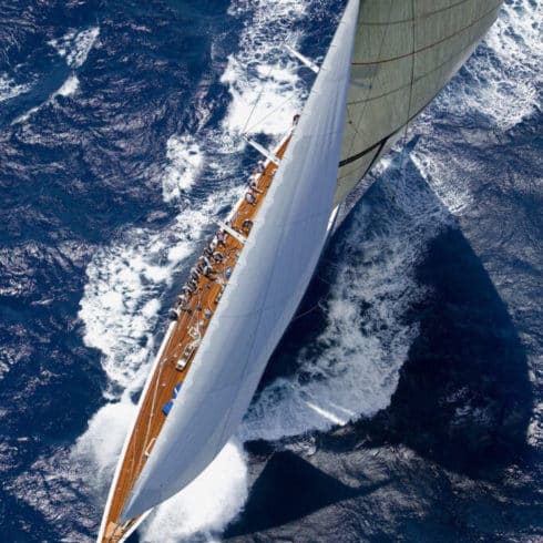 Aerial view of a large sailboat with full sails racing through ocean waters near Newport RI, creating a wake.