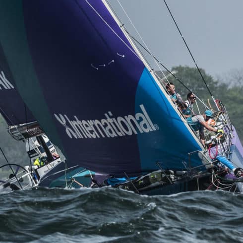 Sailing team racing a yacht with a blue sail on choppy water near Newport RI hotels.