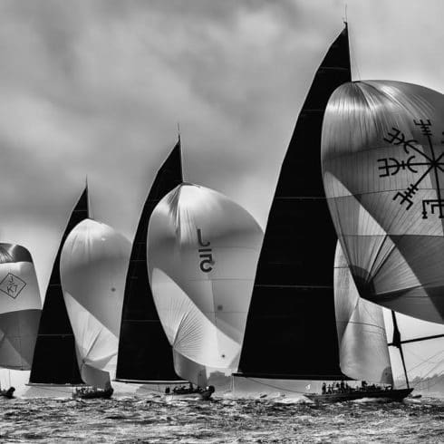 Black and white image of sailboats racing near Newport, RI, with large, billowing spinnaker sails decorated with symbols and logos.