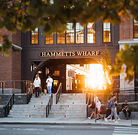 People ascending and descending stairs at the entrance of a Newport RI hotel, with a warm sunset backlighting the scene.