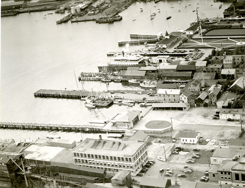 Aerial black and white historic photo of a bustling port area with docks, ships, and old buildings in Newport RI.