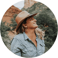 A woman in a denim shirt and hat smiles, looking upward, with a rocky landscape in the background near hotels in Newport RI.