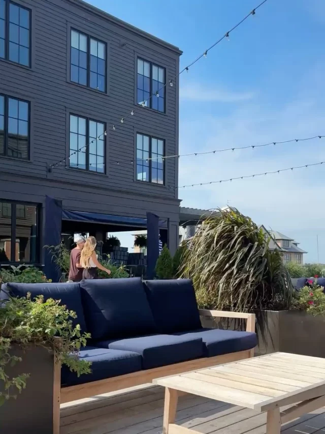 A blue couch and wooden table on a deck with a building in the background.